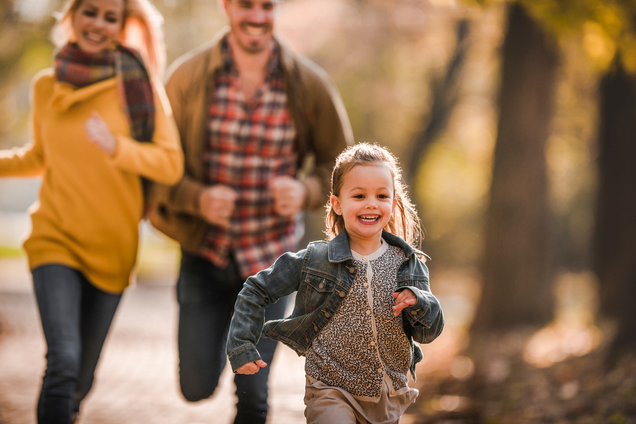 Carefree little girl having fun while being chased bu her parents in autumn day at the park.