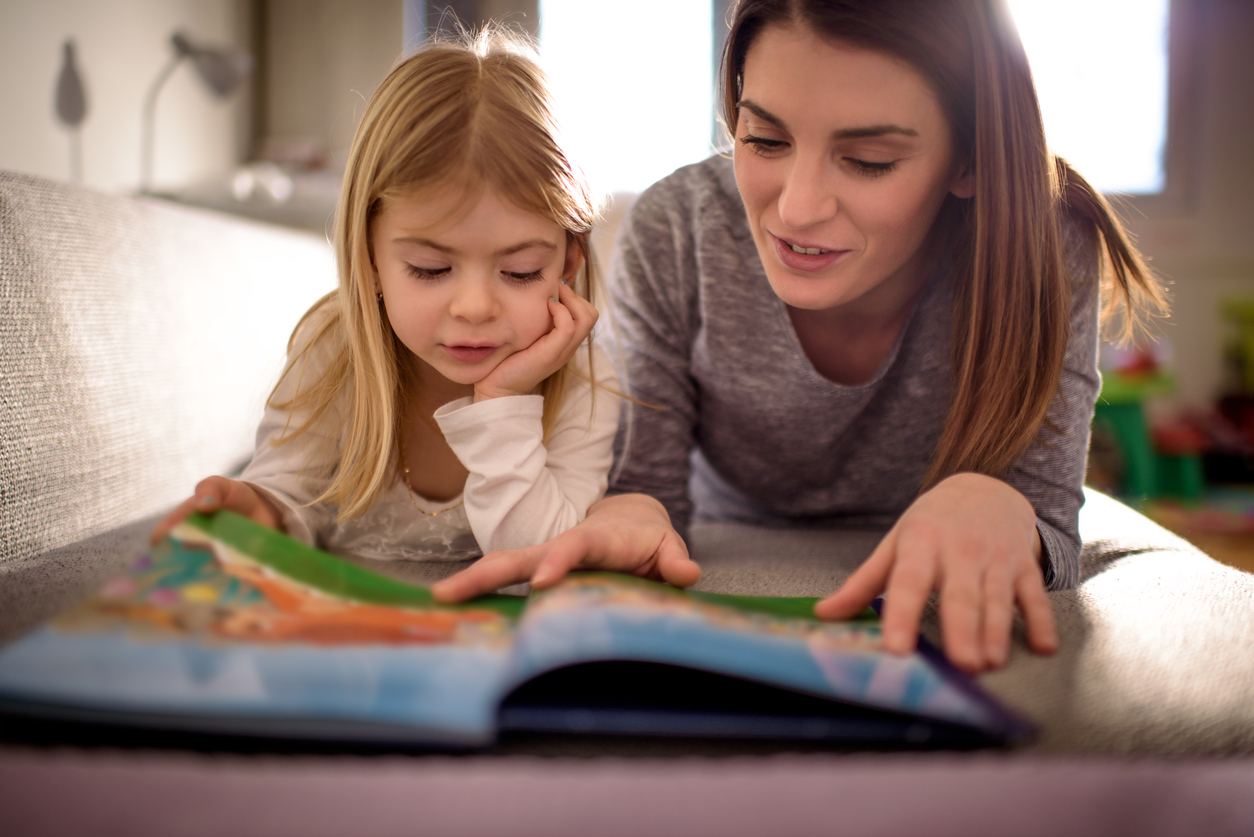  A mother and her child are lying on a couch reading a book together.